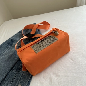 Bright orange cylinder sports crossbody bag with adjustable strap on white fabric background