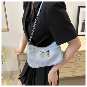 Detail of light blue satin underarm bag with silver bow and chain strap on model