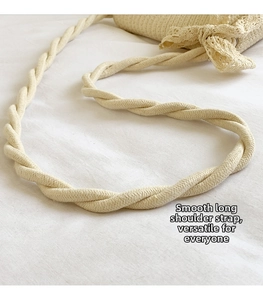Close-up of woven crossbody bag featuring cream twisted rope strap and lace bow detail