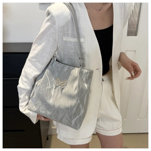 Detail of silver metallic tote bag featuring a butterfly metal logo and pleated texture
