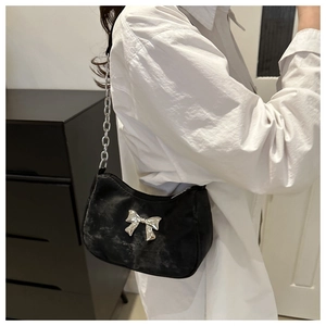 Detail of black velvet shoulder bag with silver metal bow and elegant chain strap