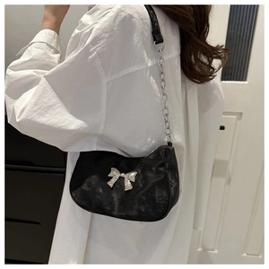 Detail of black underarm bag featuring a silver bow buckle and metal chain strap