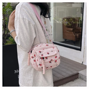 Detail of pink corduroy crossbody bag with strawberry print and woven pendant