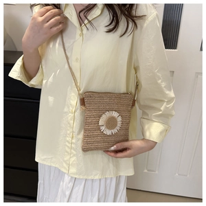 Straw woven crossbody bag with daisy flower detail worn by model in a home setting
