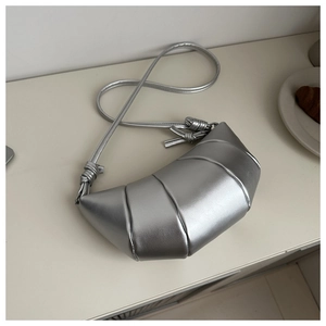 Top view of a silver croissant-shaped bag next to a real pastry on a white surface