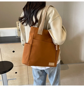 Dettaglio macro della borsa tote in tela marrone con tasca frontale ed etichetta logo