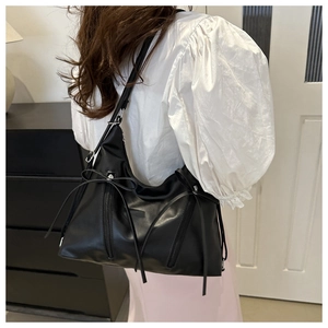 Side view of black glossy leather shoulder bag with bow details and functional zippers