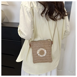 Detail of straw woven crossbody bag with white daisy flower charm and slim strap