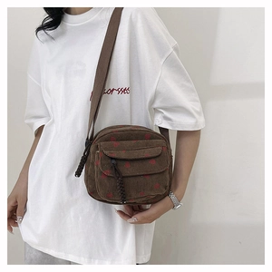 Detail of brown corduroy crossbody bag with red cherry patterns and braided zipper pull