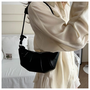 Chic black croissant bag with knotted shoulder strap shown on a model in a cozy setting