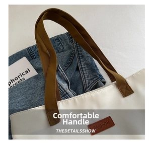 Detailed view of canvas tote bag with brown handles and fashion leather brand label