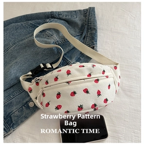 Detail view of white corduroy strawberry waist bag next to a smartphone for size reference