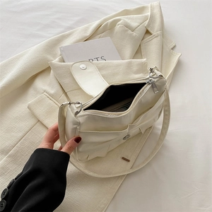 Minimalist cream white bow shoulder bag with multi-pocket design on a blazer background