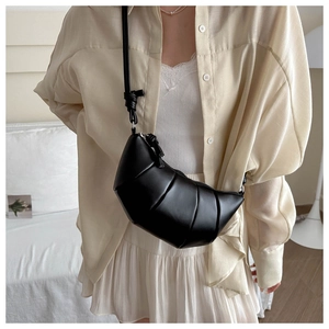 Detail of black pleated croissant shoulder bag worn by model in minimalist indoor setting