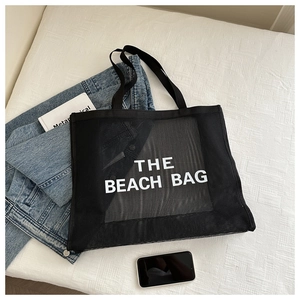 Dettaglio della borsa tote in rete nera con stampa THE BEACH BAG e manico largo