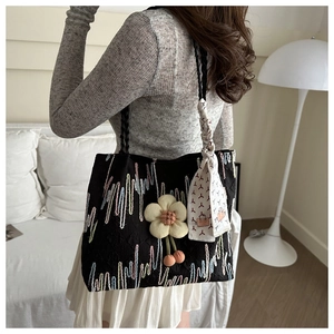 Detail of black embroidered tote bag with flower charm and silk scarf on shoulder