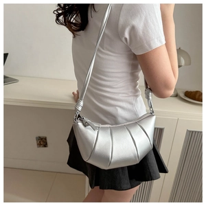 Detail of silver croissant bag featuring segmented stitching and a knotted shoulder strap