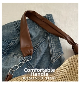 Detail of straw tote bag showing brown leather handle with chunky metal chain and ring