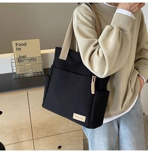 Dettaglio borsa tote in tela nera con tracolle a contrasto e nappa intrecciata decorativa