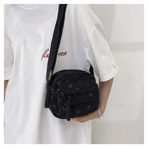 Detail of strawberry print corduroy crossbody bag worn on a white t-shirt