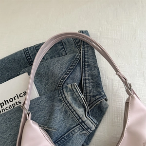 Sac à épaule minimaliste en cuir rose clair sur tissu blanc avec un jean et un livre
