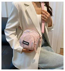 Detail of pink textured crossbody bag with fashion label and striped strap