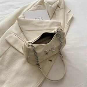 Elegant cream white underarm bag with silver bow accent and chain strap on a blazer