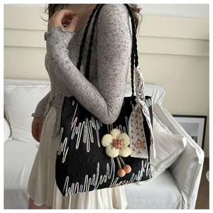 Detail of black tote bag with wavy embroidery, floral pendant and decorative silk scarf