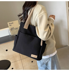Dettaglio della borsa tote in tela nera con tasche laterali e etichetta in pelle