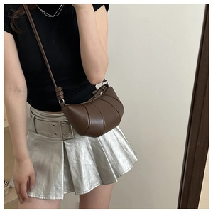 Detail of a croissant bag with vertical pleats and leather strap on a model