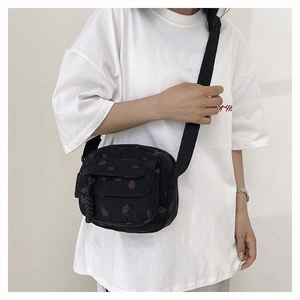 Detail of black corduroy crossbody bag with strawberry print and woven zipper puller