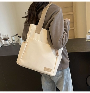 Dettaglio della borsa tote in tela con tracolla larga marrone e toppa in pelle al caffè