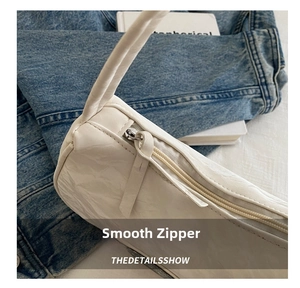 Detailed close-up of smooth silver zipper and pleated texture on a white nylon underarm bag