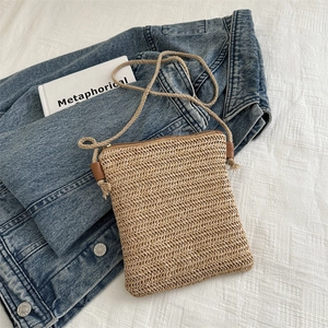 Minimalist straw crossbody bag with zipper and rope strap on denim background