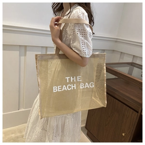 Dettaglio della borsa da spiaggia beige a rete con stampa THE BEACH BAG e manici