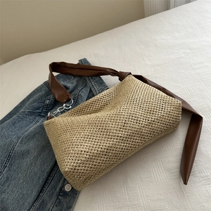 Minimalist straw shoulder bag with dark brown leather strap and silver chain on bedsheet