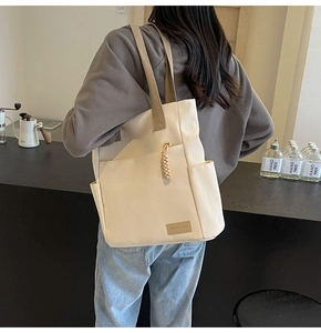 Dettaglio della borsa tote in tela crema con etichetta in pelle e ciondolo intrecciato