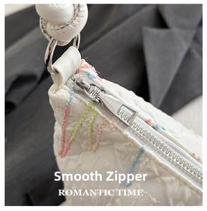 Close-up of white embossed tote bag with colorful decorative stitching and silver zipper