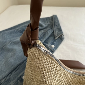 Straw shoulder bag with brown leather knotted handles and silver zipper on blue denim
