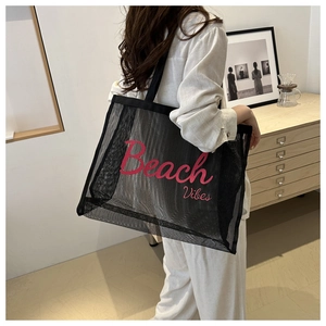 Dettaglio della borsa tote nera in rete con scritte Beach Vibes rosa indossata