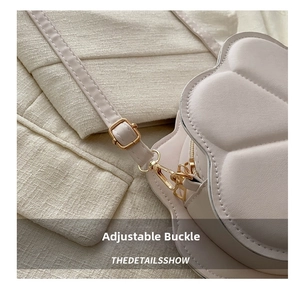 Detail view of the adjustable metal buckle and golden spring hook on a cream crossbody bag