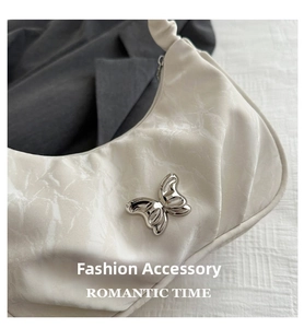Detail of cream white pleated crescent bag featuring a silver metal butterfly ornament