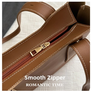 Detail of premium brown leather handbag featuring golden metal zipper and contrast stitching