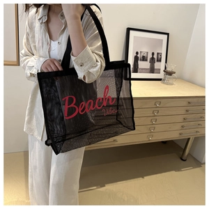 Dettaglio borsa tote in rete nera con scritta Beach Vibes rossa in una stanza