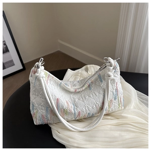 Close-up of quilted white handbag with colored embroidery and knotted rope strap detail