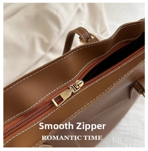 Détail de la fermeture éclair dorée et coutures blanches sur le sac fourre-tout marron