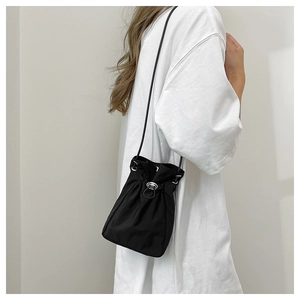 Detail of minimalist black drawstring crossbody bag with silver metal lock and nylon texture