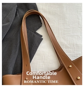 Detail of caramel leather tote bag reinforced straps with gold rivets and precision stitching