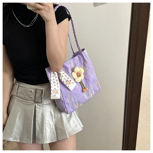 Detailed texture of purple quilted canvas tote with floral charm and patterned silk scarf