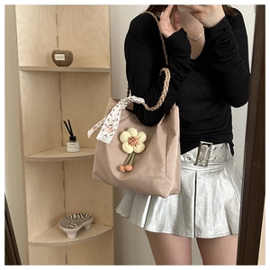 Detail of beige tote bag with a 3D knit flower charm and decorative silk scarf on handle